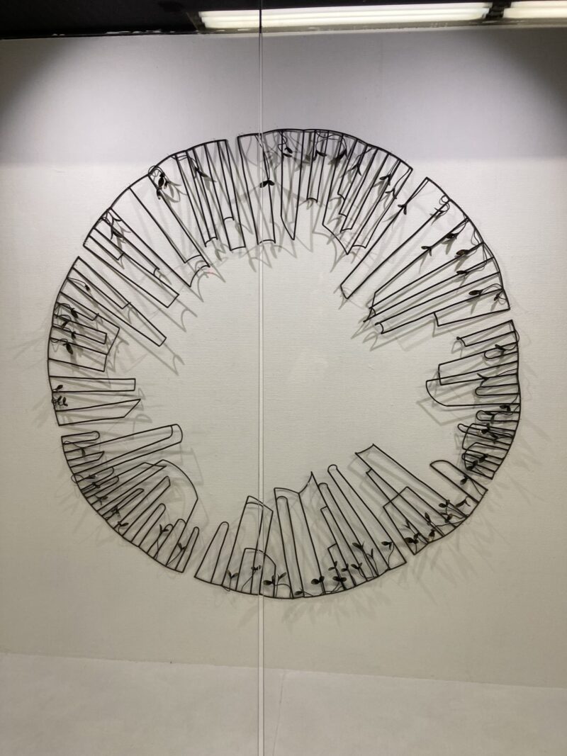 佐藤あゆみ「覗く」壁面に設置された円形の鉄製アート作品の全体像。穴から外のビルを覗いているように見える。